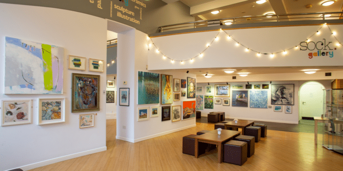 Interior of the Sock Gallery. Posters and art work are on the cream walls and fairy lights are lit up along the walls.