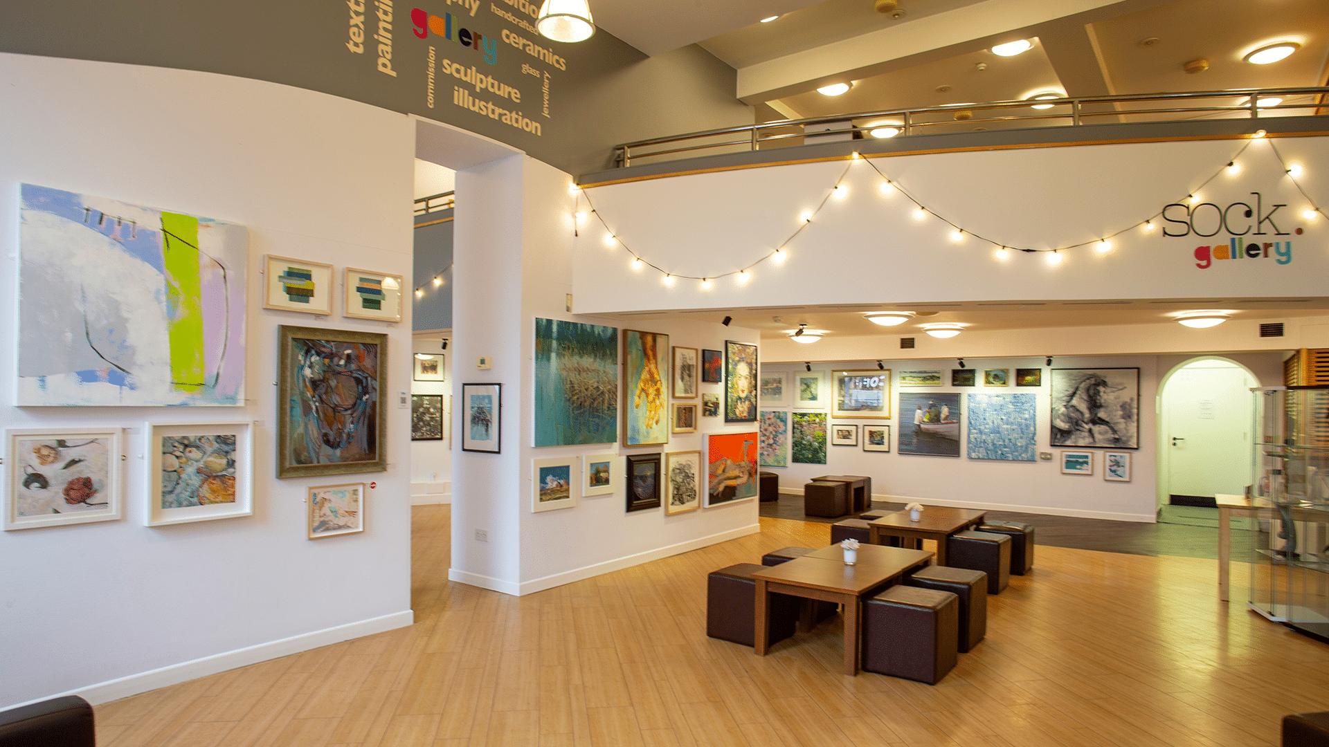 Interior of the Sock Gallery. Posters and art work are on the cream walls and fairy lights are lit up along the walls.