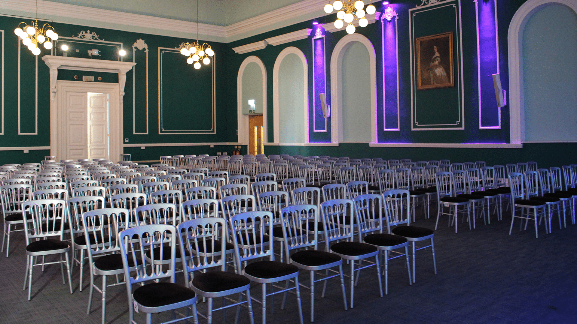 Interior of the Victoria Room. The room is set up for a wedding with rows of white chairs going to the back of the room, the walls are green with white panelling.